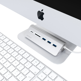 Un hub USB argenté avec un clavier blanc et un ordinateur Mac. Le hub possède des ports USB et un lecteur de carte.