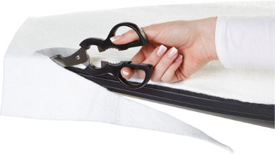 Une main tenant des ciseaux noirs coupant du tissu blanc sur une surface noire.