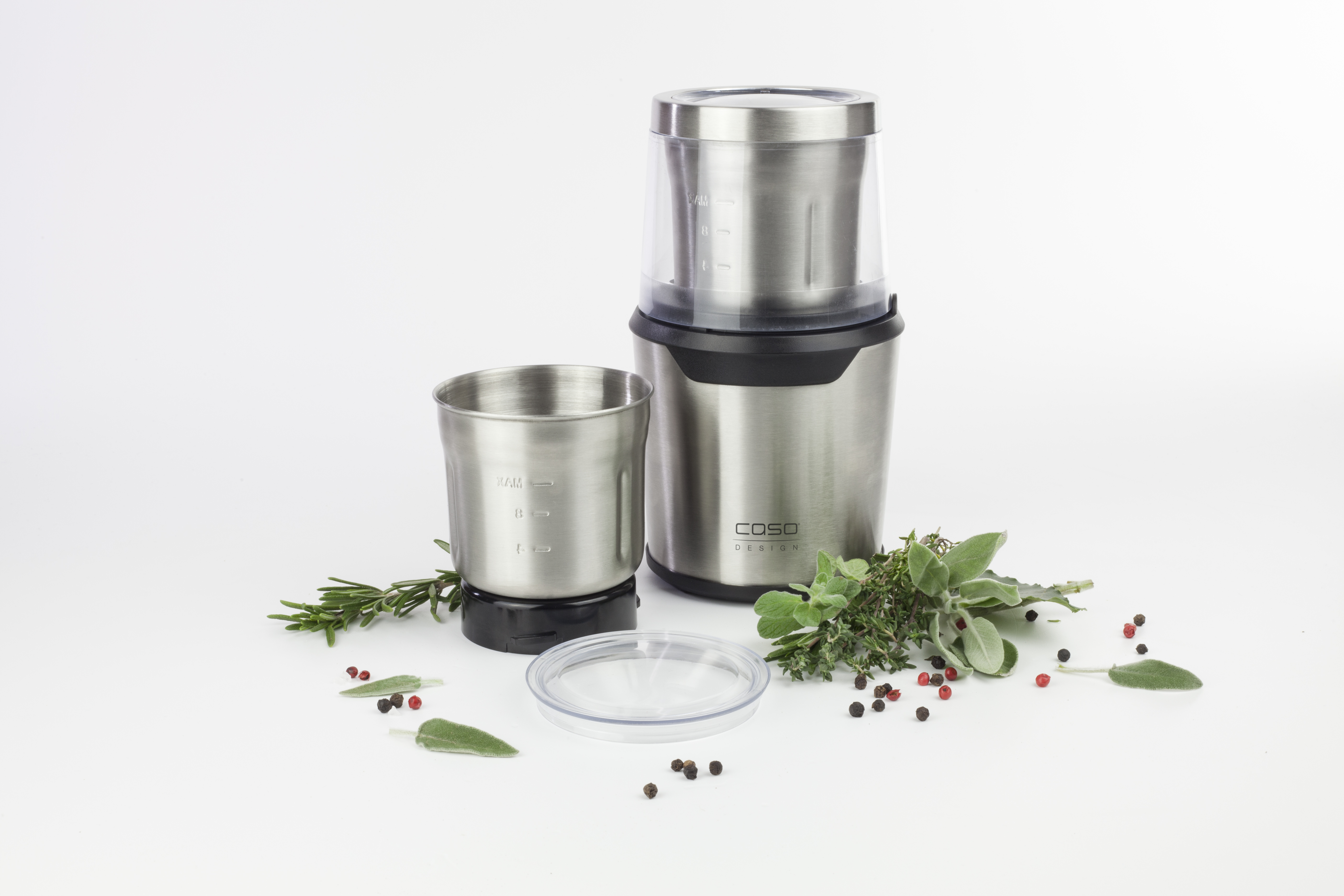 Edelstahl-Mühle mit durchsichtigem Deckel und separater Tasse. Kräuter und Pfefferkörner vorhanden.
