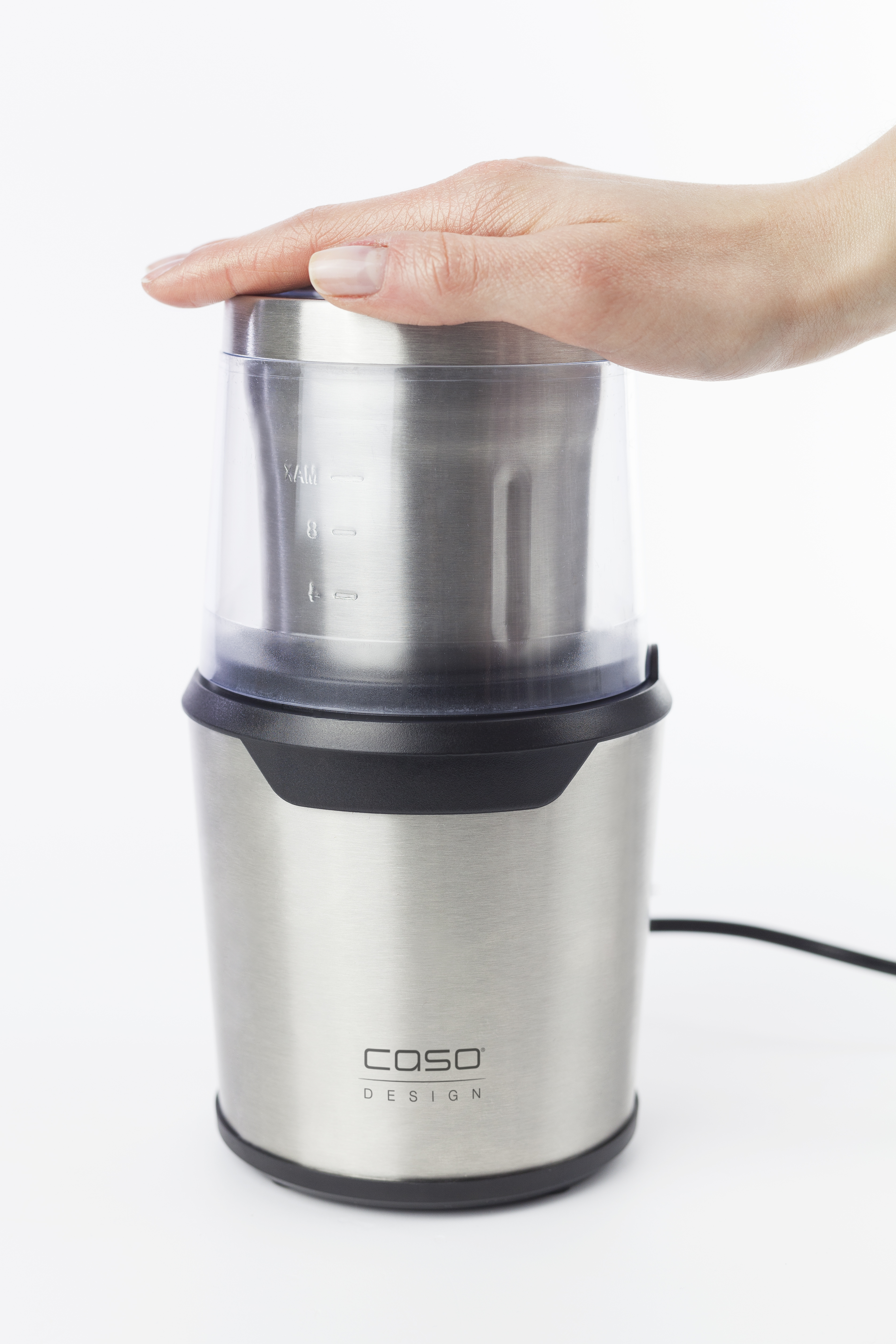 Eine Hand setzt einen transparenten Deckel auf eine Kaffeemühle aus Edelstahl. Die Mühle ist am Fuß schwarz.
