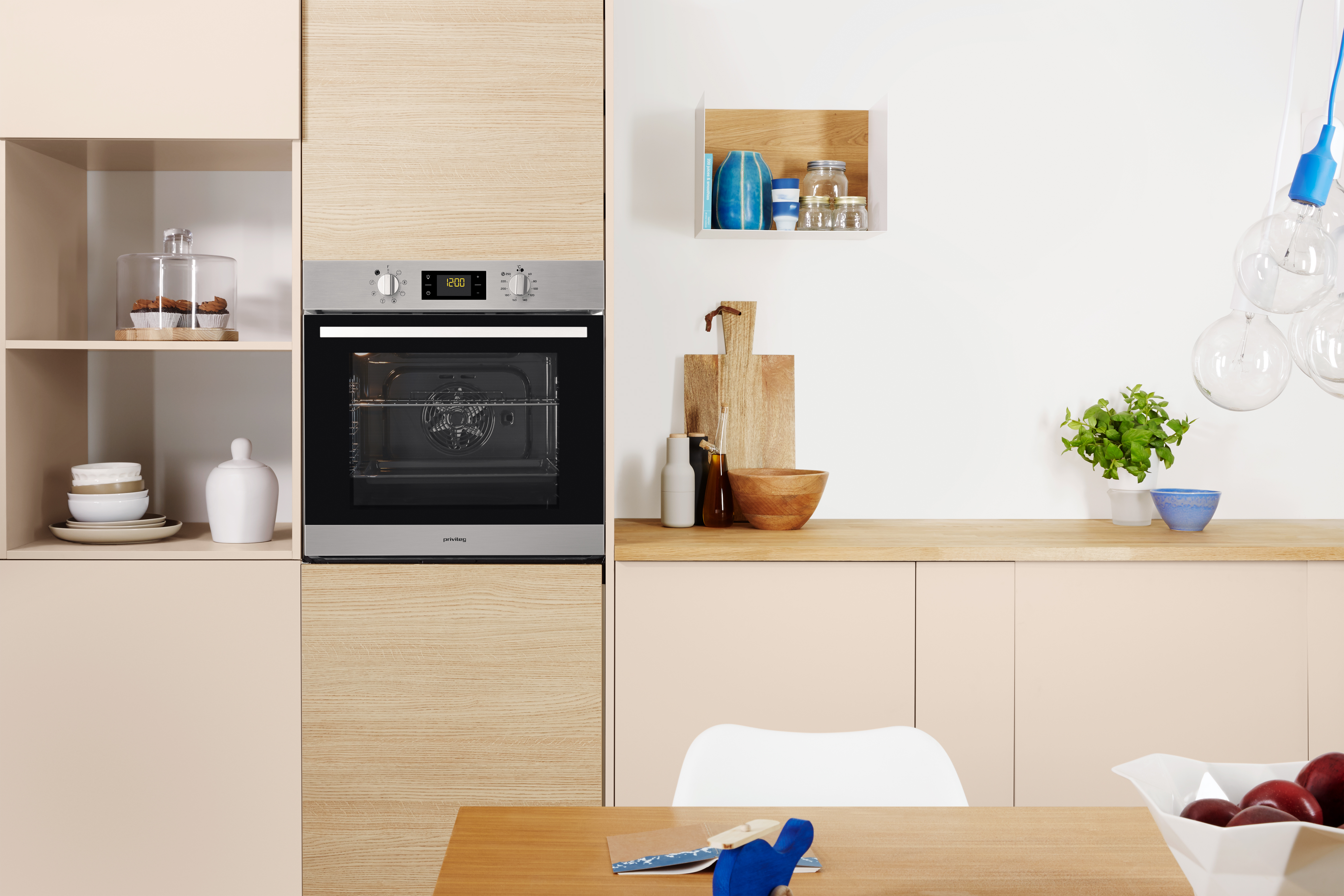 Moderne Küche mit Backofen und Schränken. Ein Tisch mit Schüssel und Pflanzen im Vordergrund.