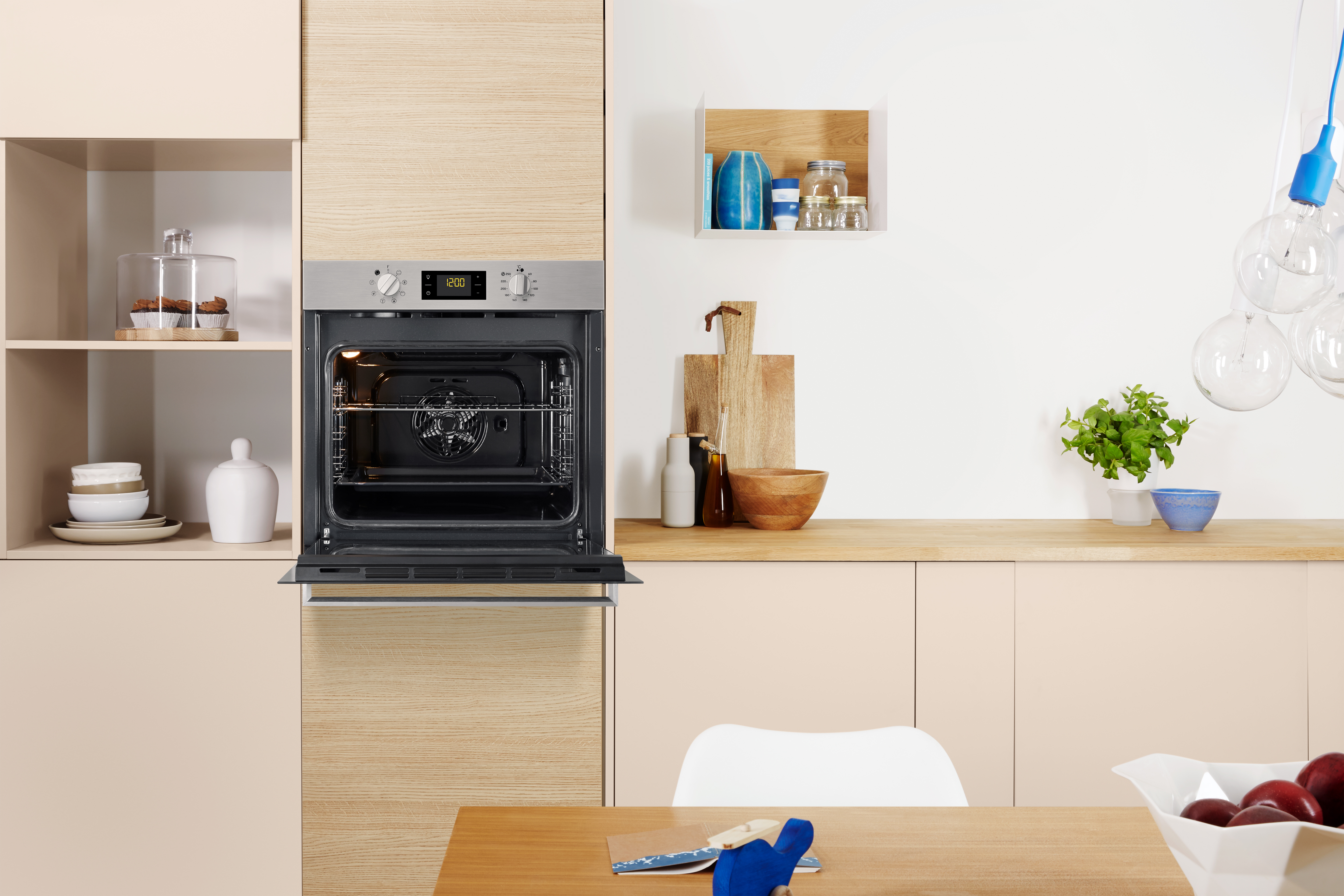 In der Küche installierter Ofen, Tür offen, Innenraum und Lüfter zeigend. Küche beige mit Holztisch.