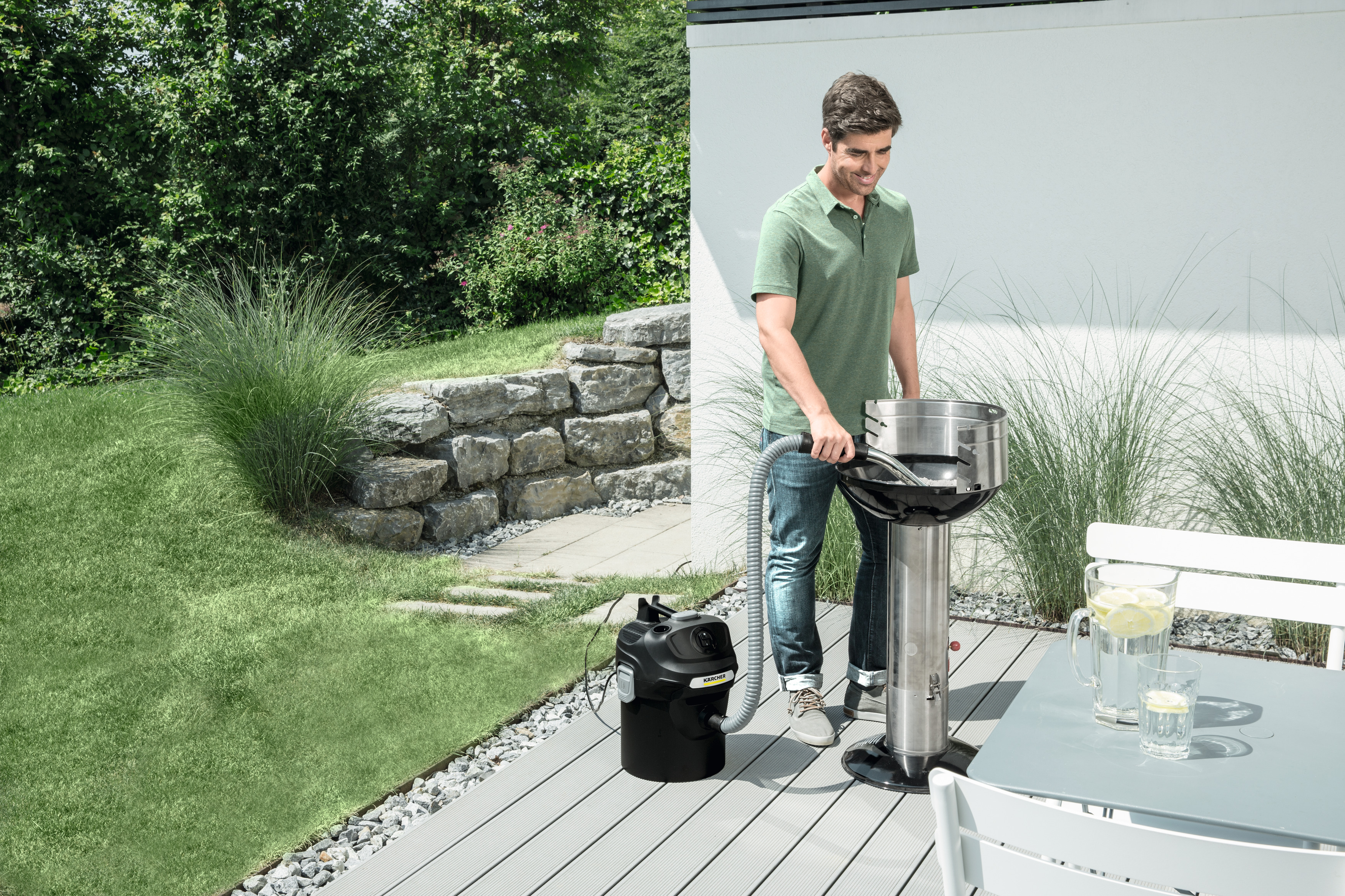 Ein Mann grillt auf einer Terrasse. Ein schwarzer Staubsauger ist im Hintergrund.