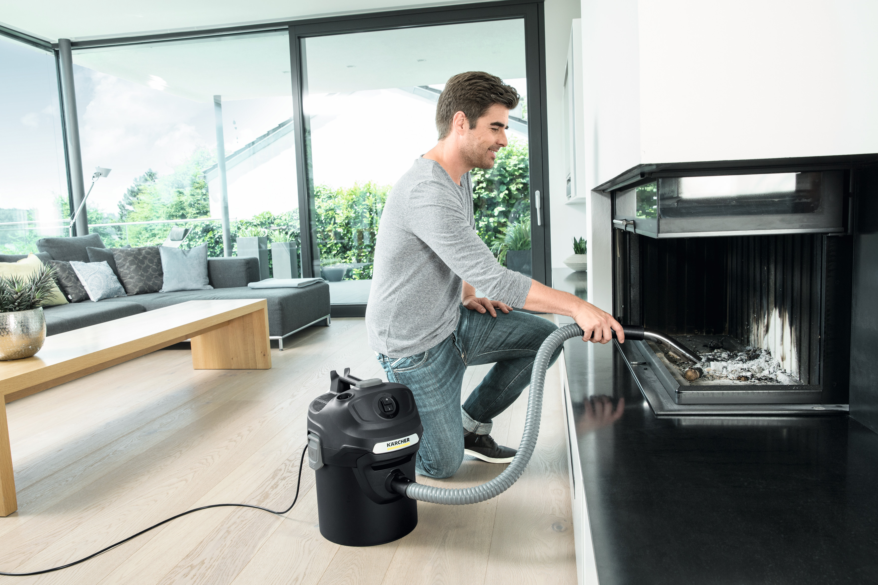 Ein Mann reinigt einen Kamin mit einem Staubsauger. Der Kamin ist schwarz, der Raum modern.