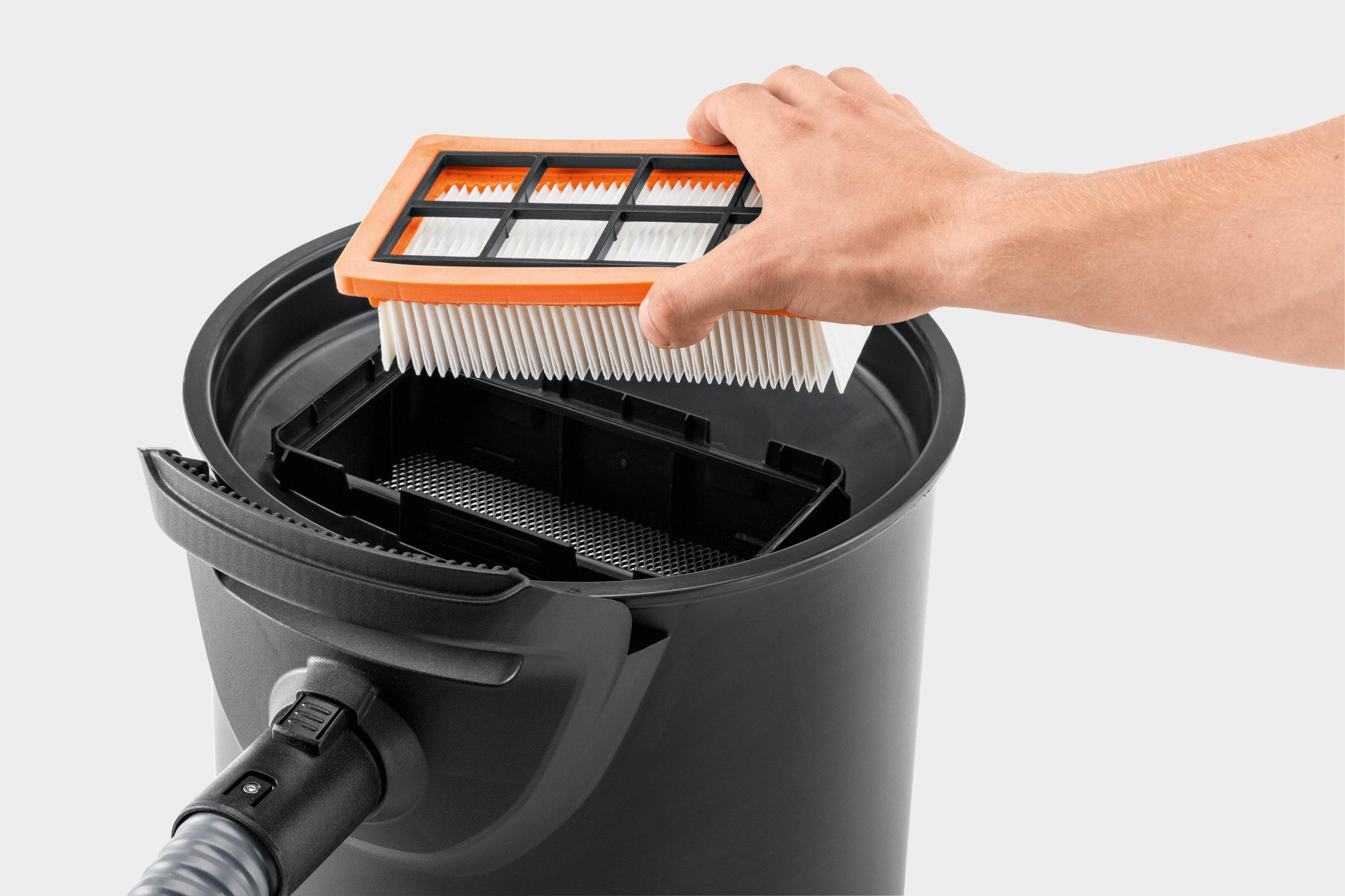 Hand, die einen orangefarbenen und weißen Filter in einen schwarzen Staubsaugerbehälter einsetzt.