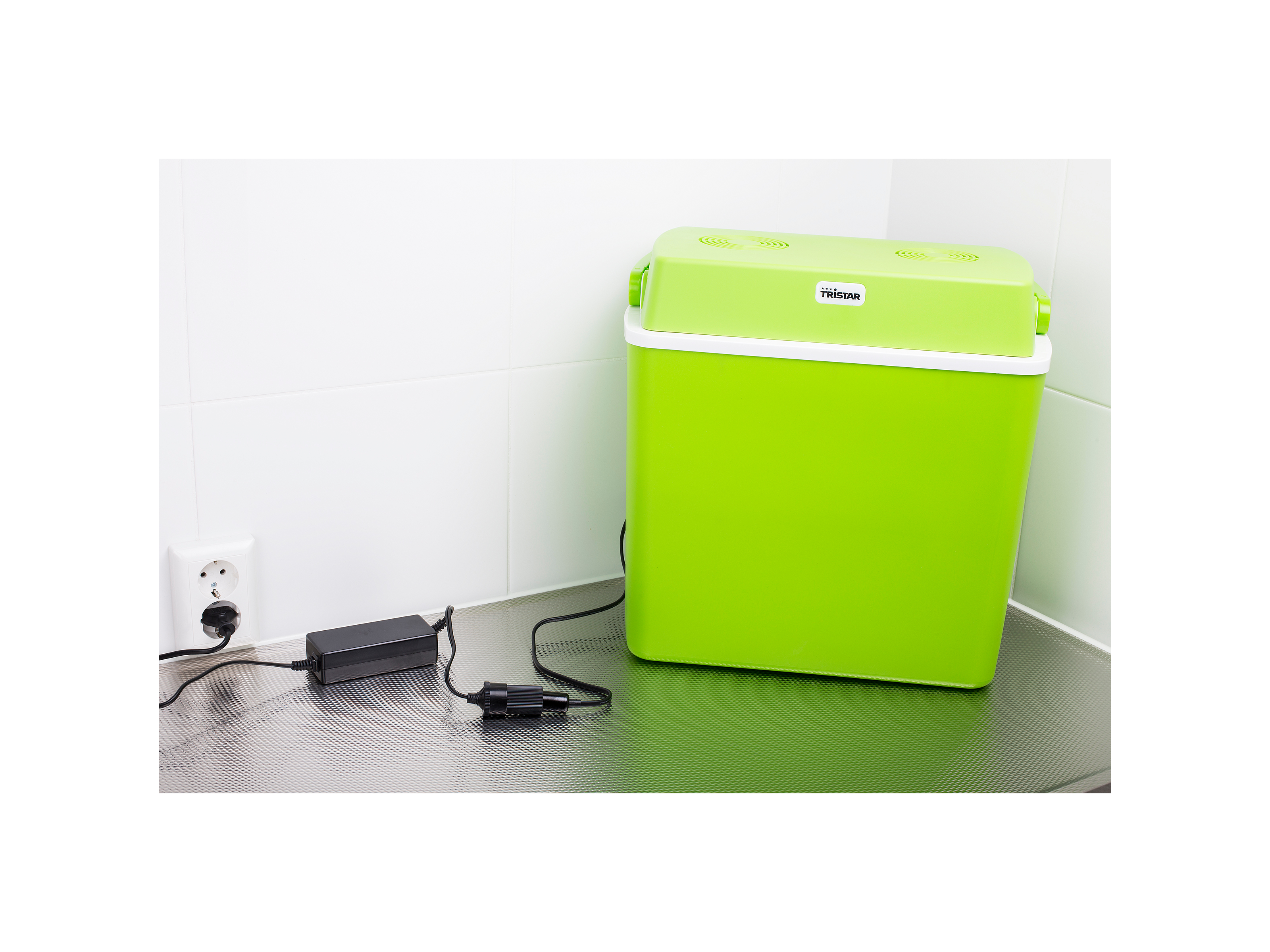 Eine grüne Kühlbox, die an eine Steckdose und einen Netzadapter angeschlossen ist. Auf einer grauen Arbeitsplatte platziert.