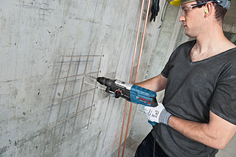 Férfi Bosch fúrót használ betonon, védőszemüveggel és kesztyűvel.