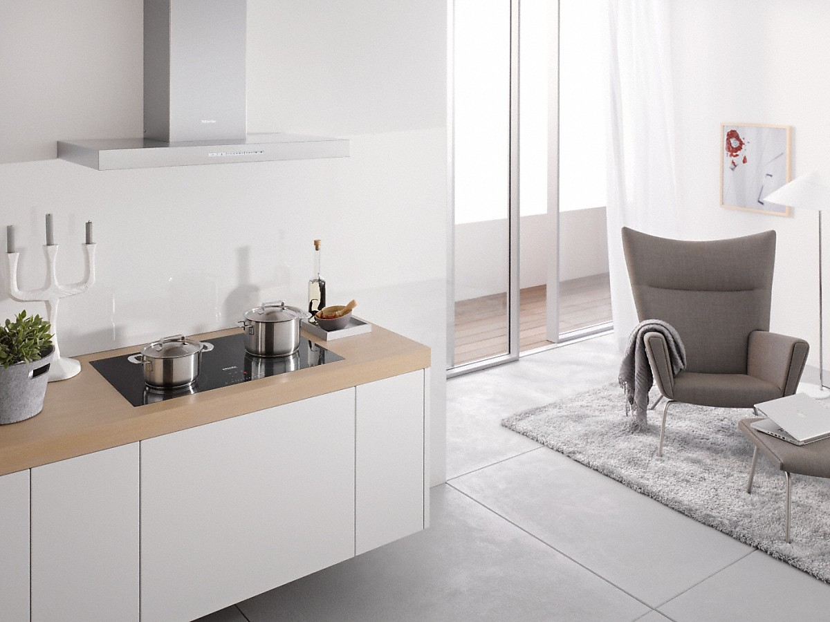 Moderne Küche mit Induktionskochfeld, Töpfen und einem grauen Sessel im Hintergrund.