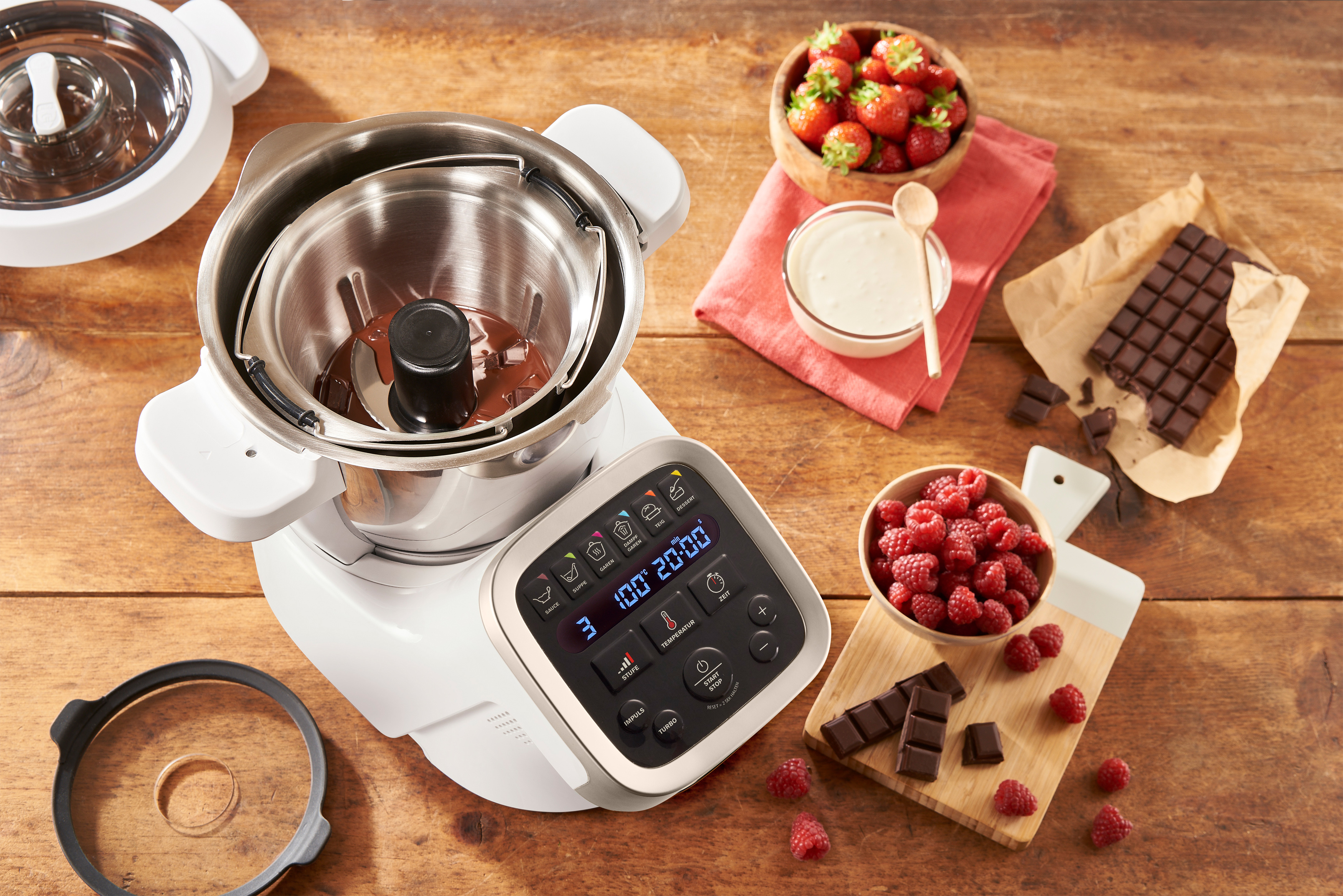 Eine weiße Küchenmaschine mit Bildschirm und Zutaten wie Schokolade und Beeren.