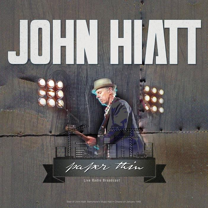 Albumhoes van 'John Hiatt - Paper Thin'. Een man speelt gitaar, met een podium en lichten op de achtergrond.