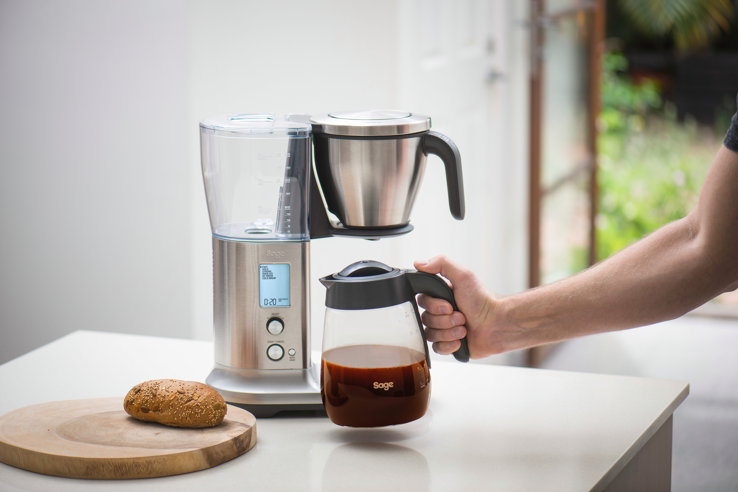 Eine silberne Kaffeemaschine mit einer Glaskaraffe, die von einer Hand gehalten wird.