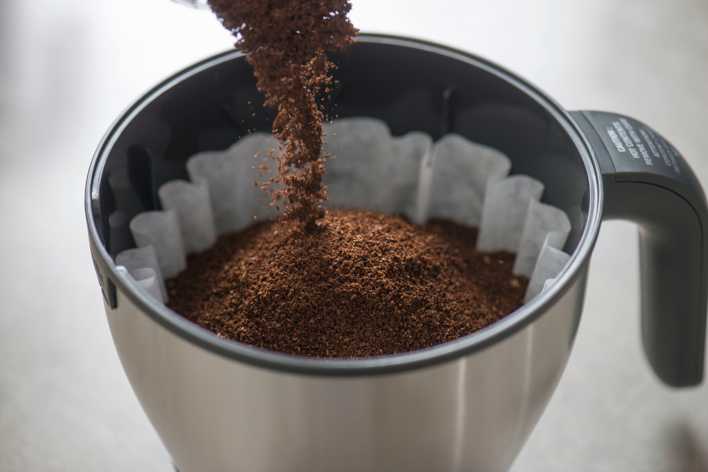 Gemahlener Kaffee, der in einen Kaffeefilter gegossen wird, mit Filterpapier in einer Edelstahl-Kaffeemaschine.
