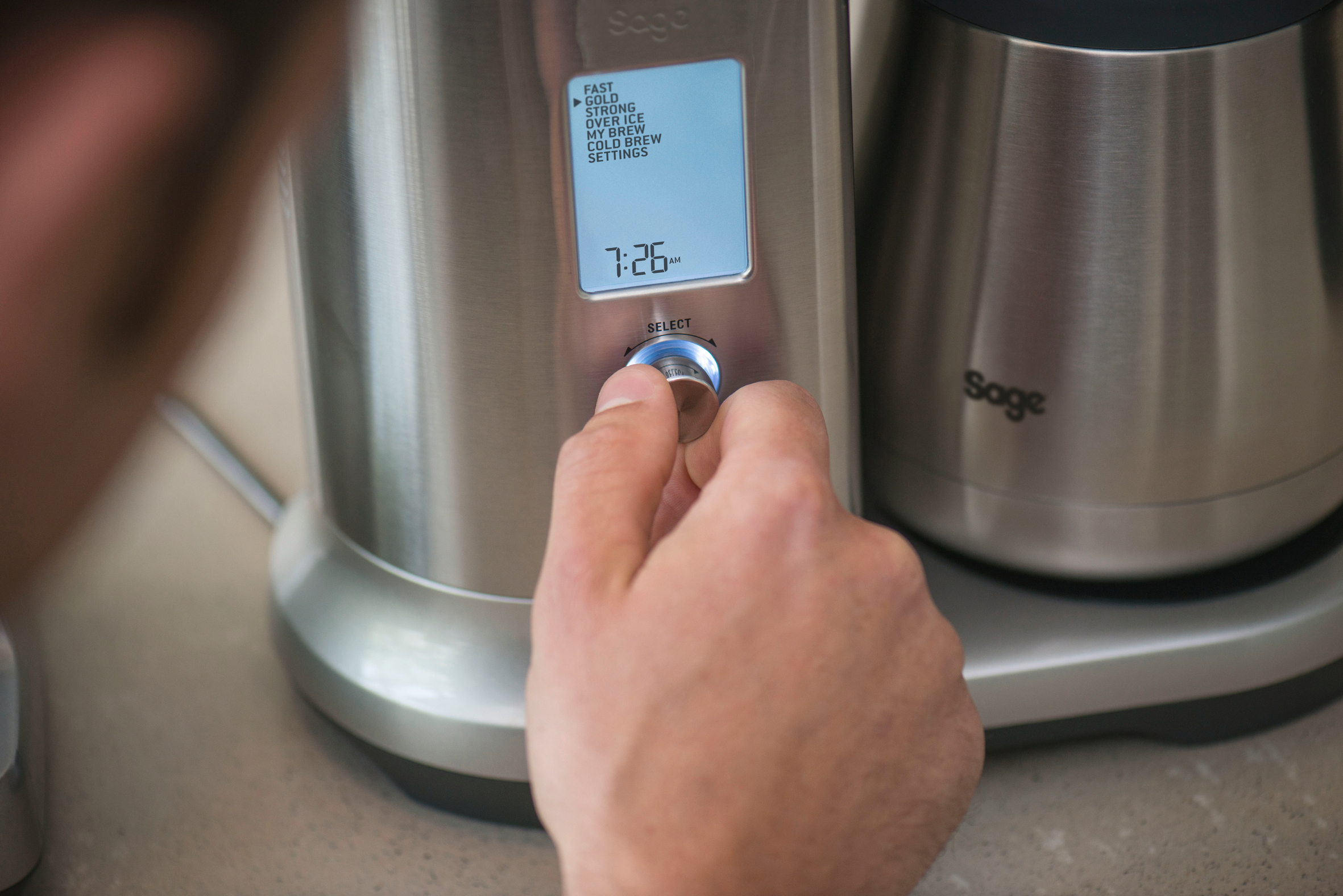 Die Hand einer Person drückt eine Taste an einer silber-schwarzen Kaffeemaschine.