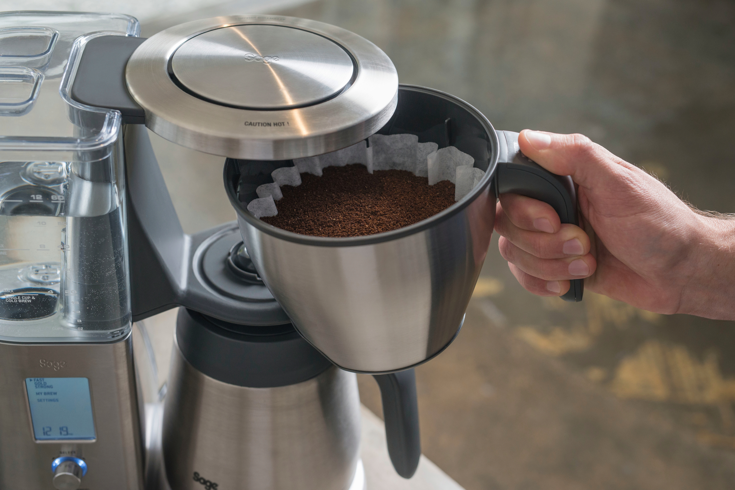 Eine Person nimmt einen Filterkorb aus einer Kaffeemaschine.