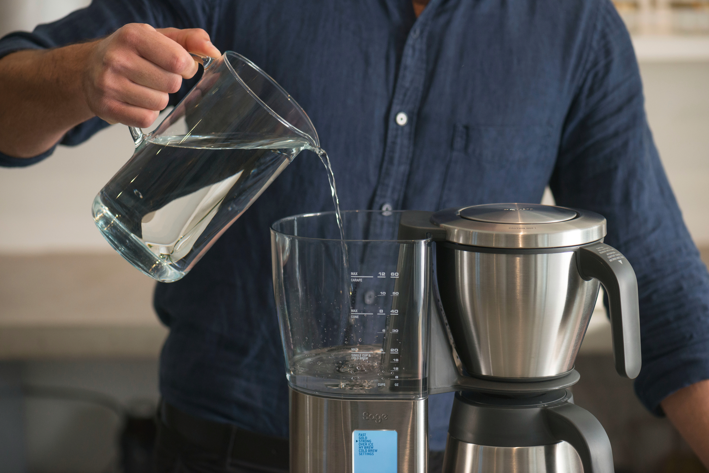 Eine Person gießt Wasser aus einem Glaskrug in eine Kaffeemaschine.