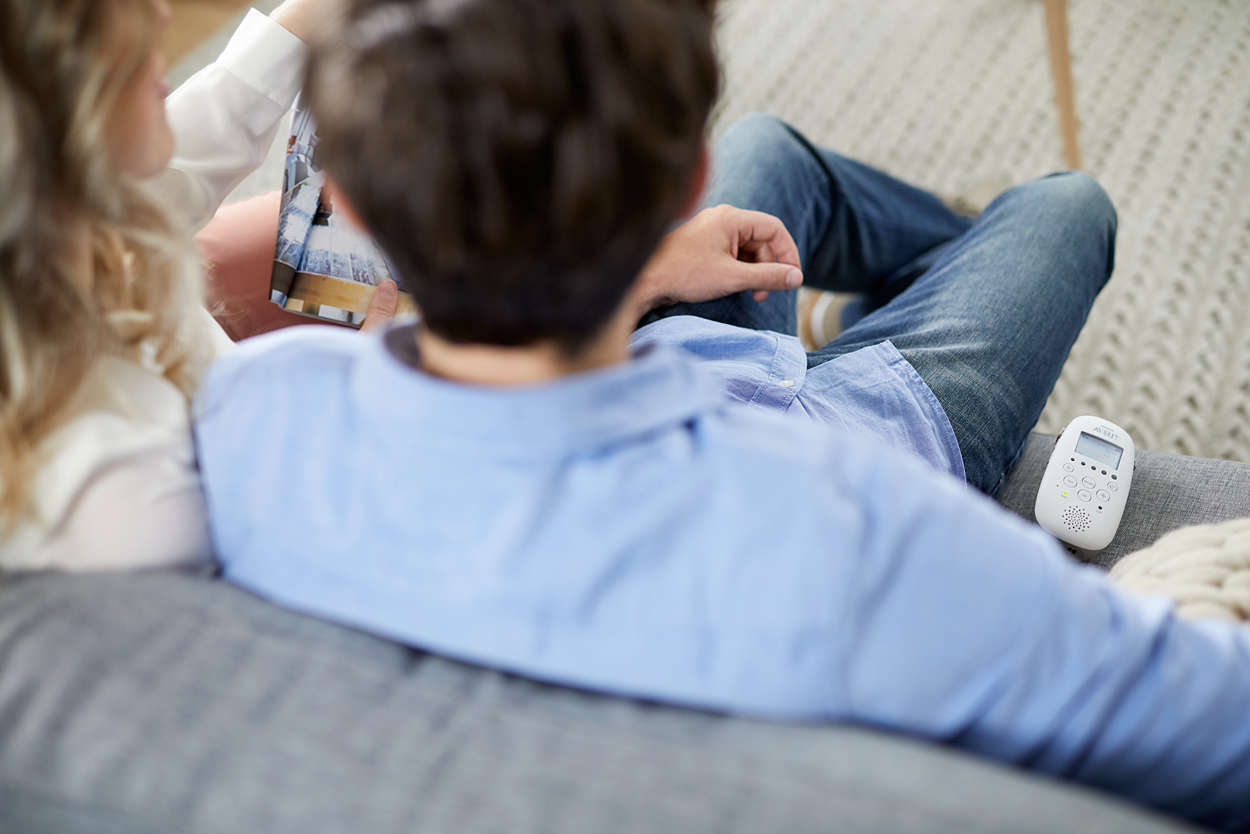 Zwei Personen auf einem Sofa betrachten ein Fotoalbum, daneben liegt ein Babyphone.