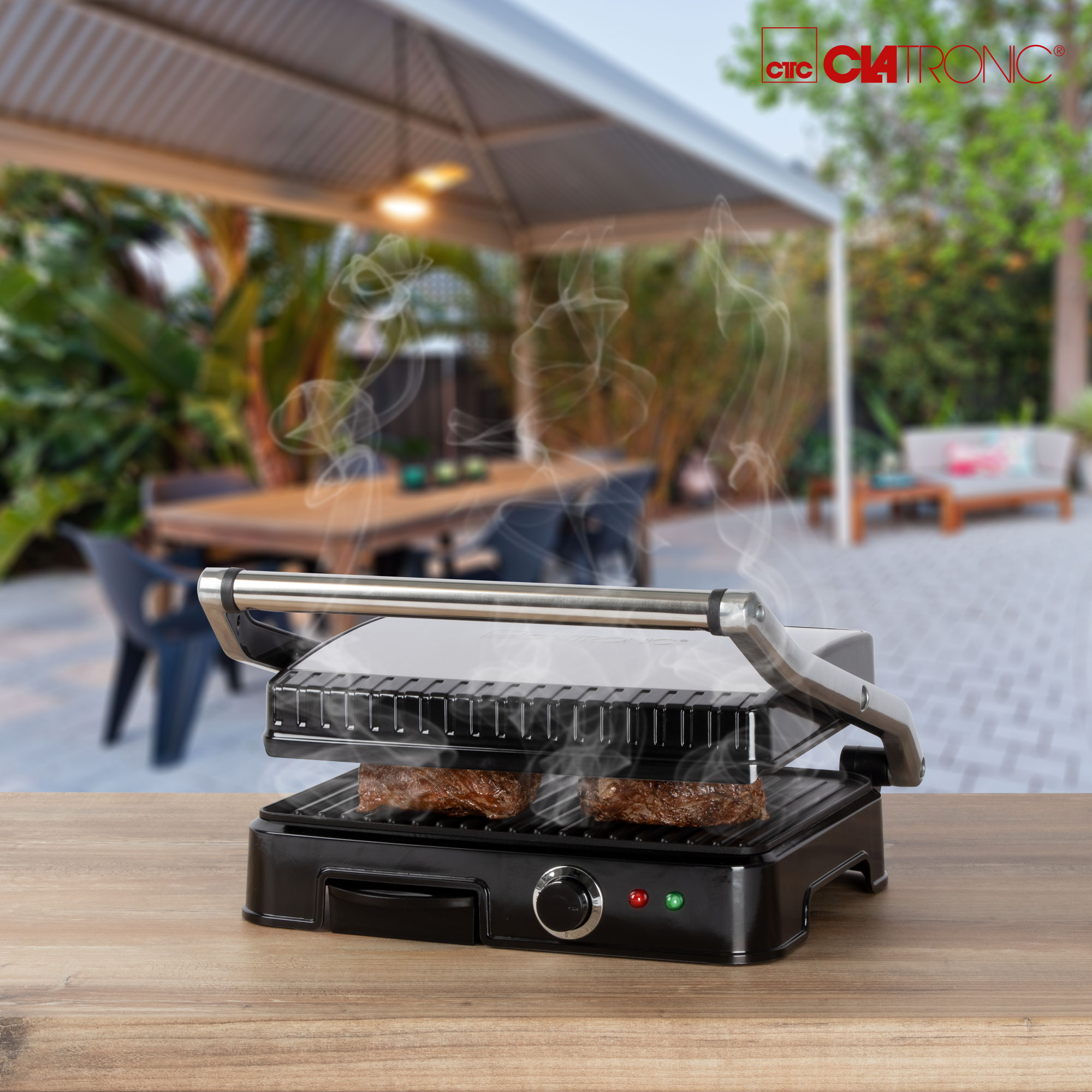 Ein Grill mit zwei Steaks und Dampf im Hintergrund; ein Holztisch im Vordergrund.
