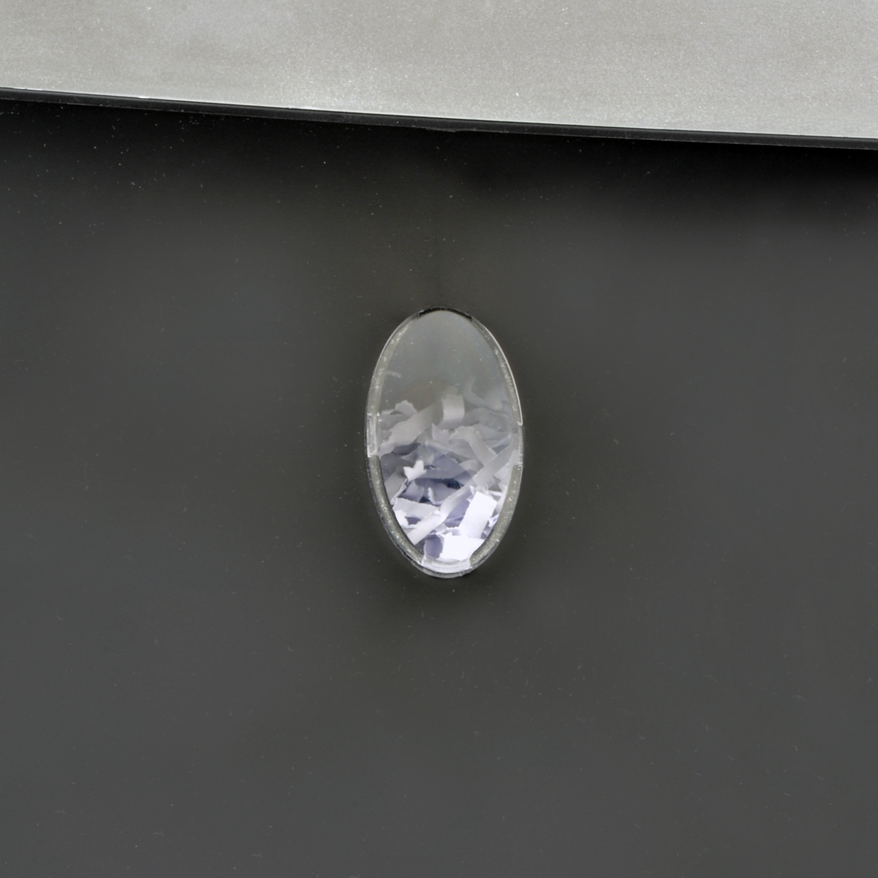 Close-up of a dark gray surface with an oval, silver-framed, crystal-like accent in the center.