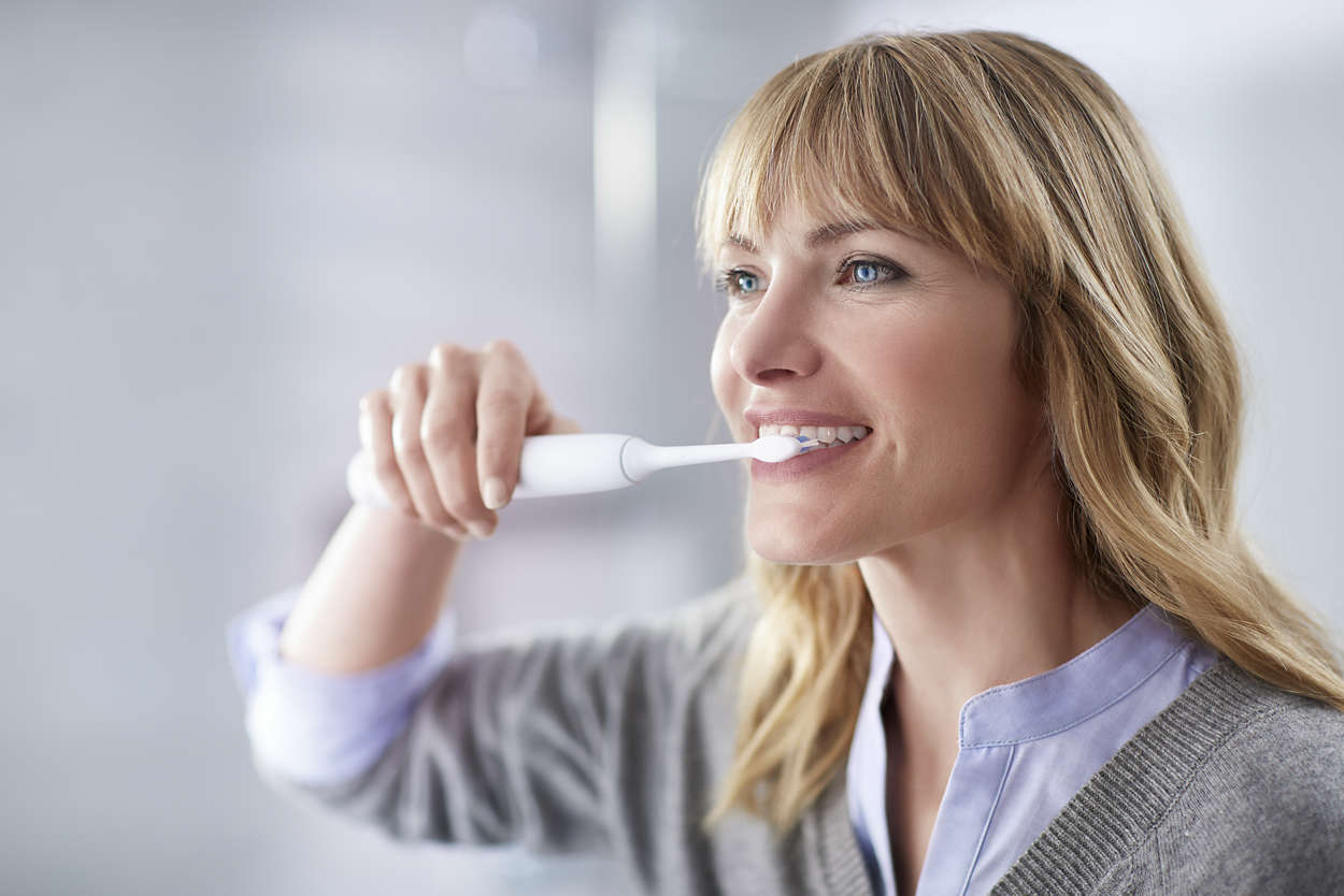 Une femme se brossant les dents avec une brosse à dents électrique.
