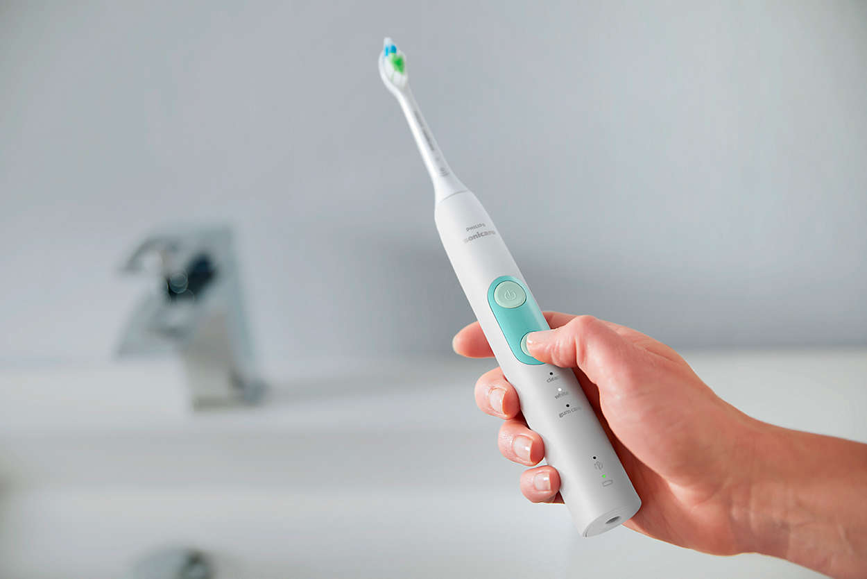 Une main tient une brosse à dents électrique blanche. La tête a des soies bleues et vertes.
