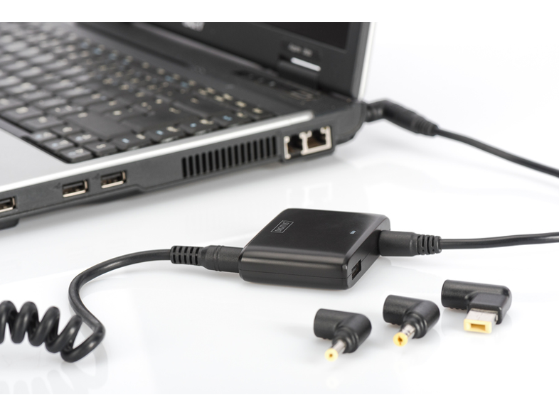 Laptop, hálózati adapter és különböző tápcsúcsok fehér felületen.