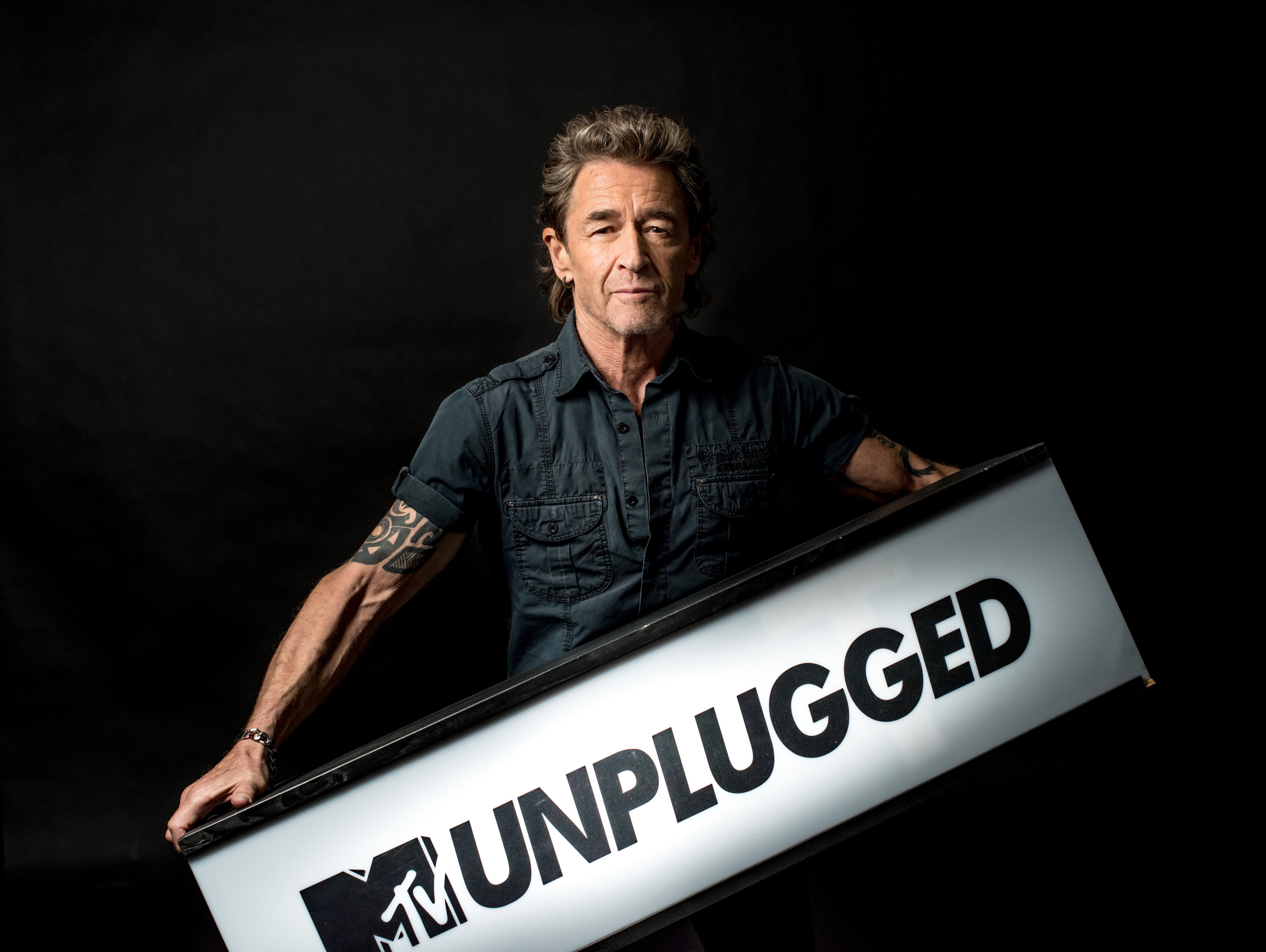 Mann hält ein Schild mit MTV Unplugged auf schwarzem Hintergrund.