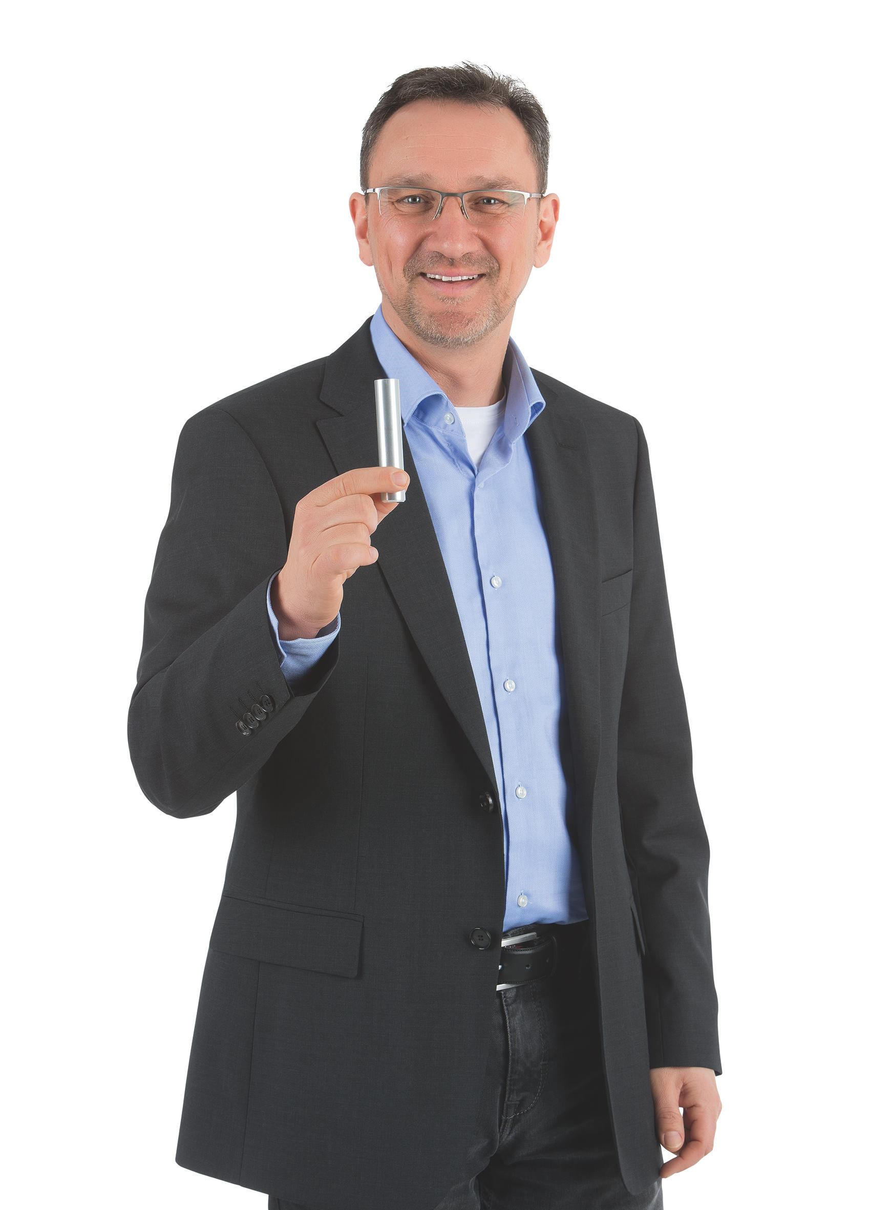 Ein Mann im Anzug hält einen silbernen Zylinder und lächelt in die Kamera.
