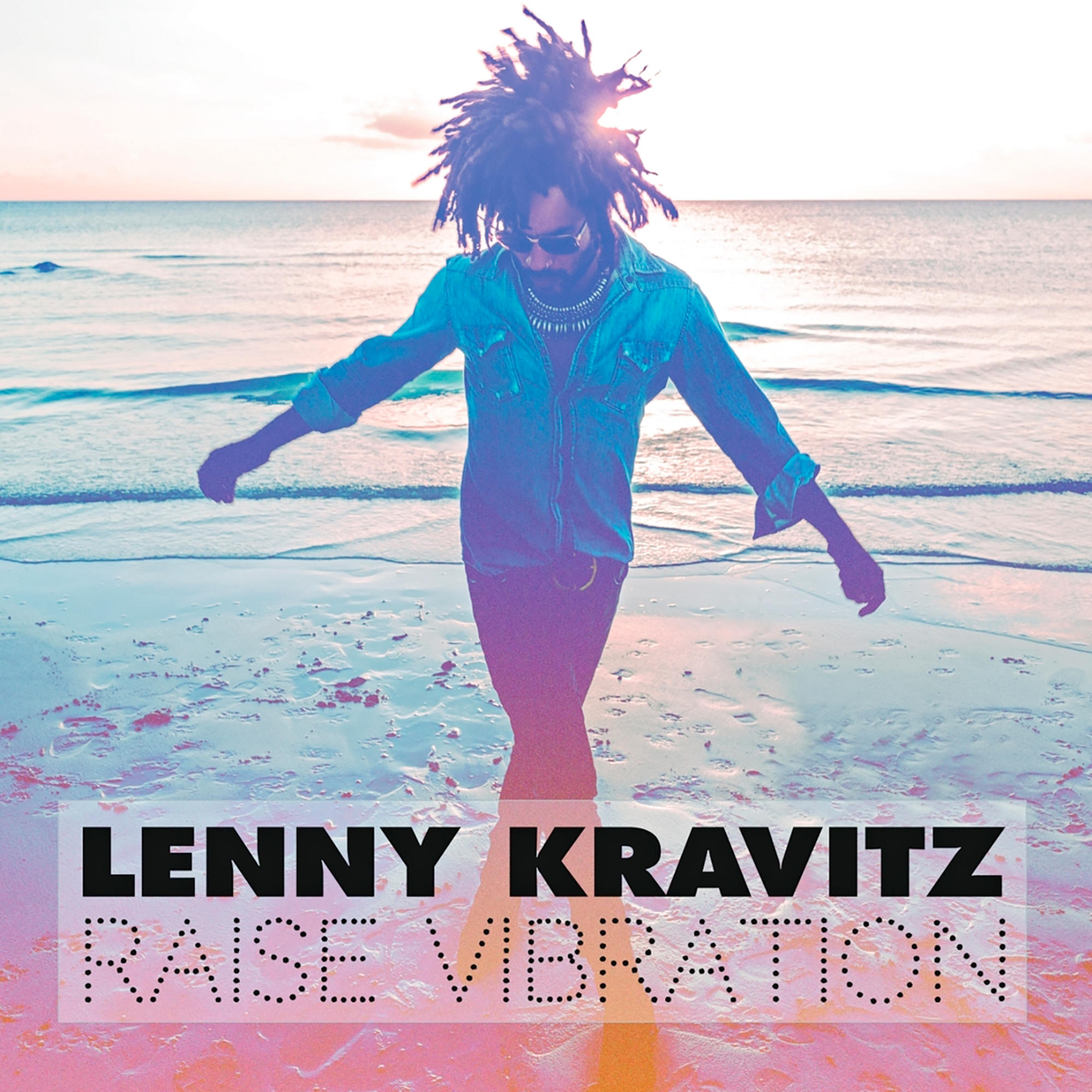 Lenny Kravitz sur une plage. Il porte des lunettes de soleil et du denim. Texte 'RAISE VIBRATION' en bas.