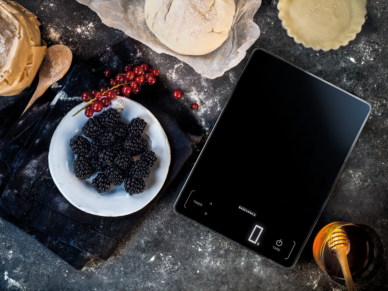 Eine schwarze digitale Küchenwaage mit Zutaten wie Beeren und Teig.