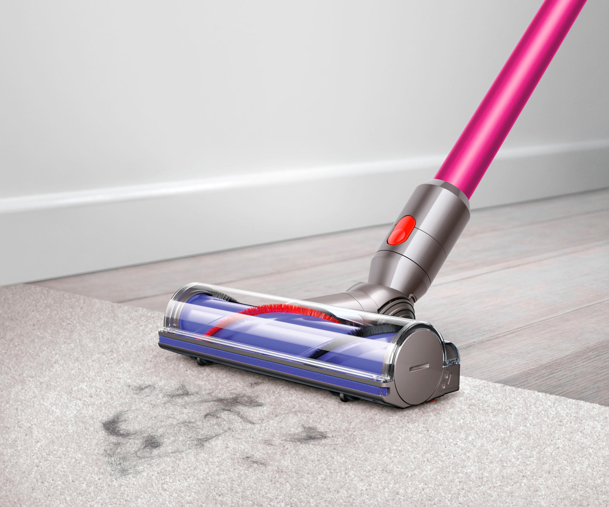 Dyson Staubsaugerkopf auf Teppich. Rosa und silberner Staubsauger. Grauer Teppich und weiße Wand.