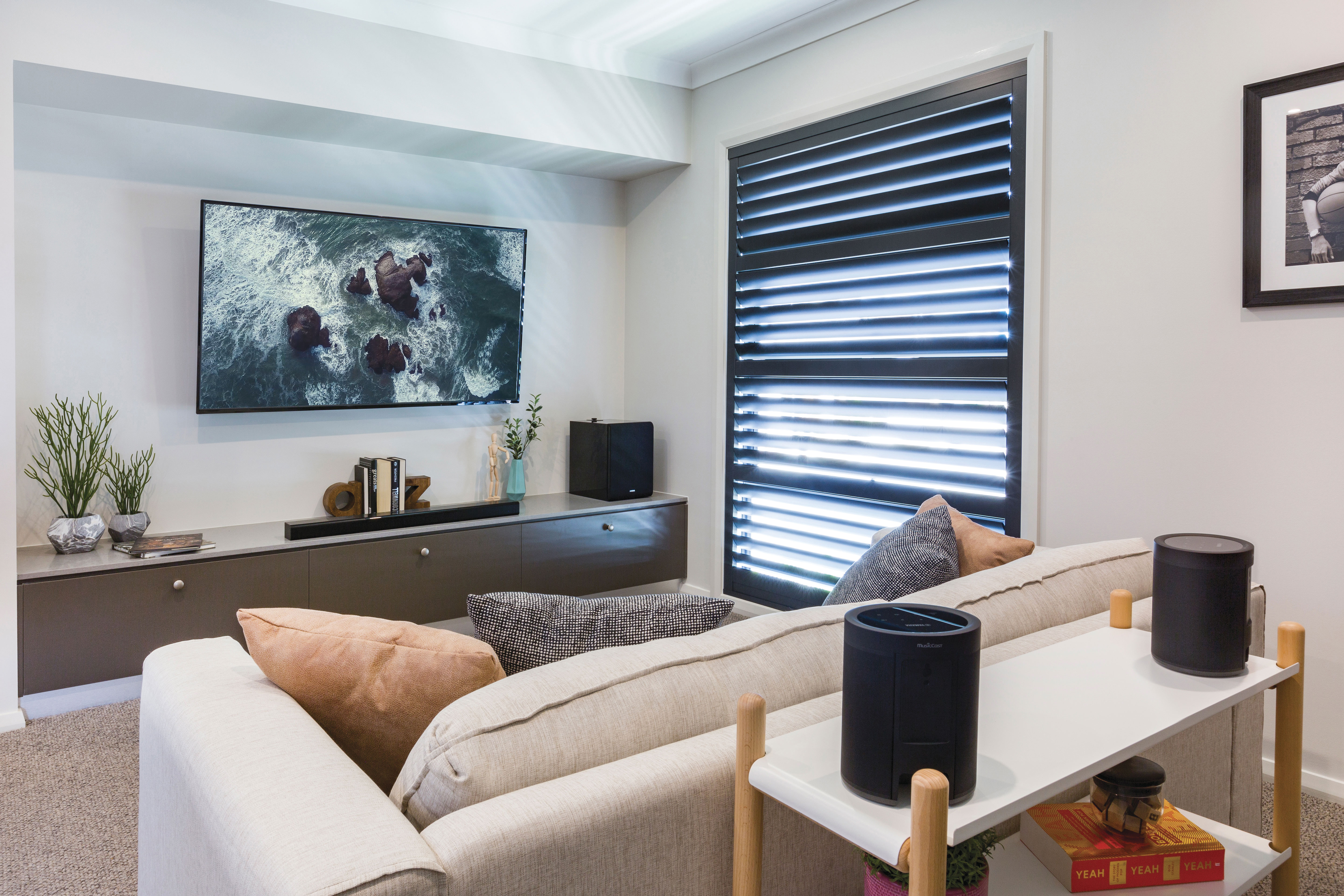 Modernes Wohnzimmer mit großem Fernseher, Sofa und Lautsprechern, mit Sonnenlicht.