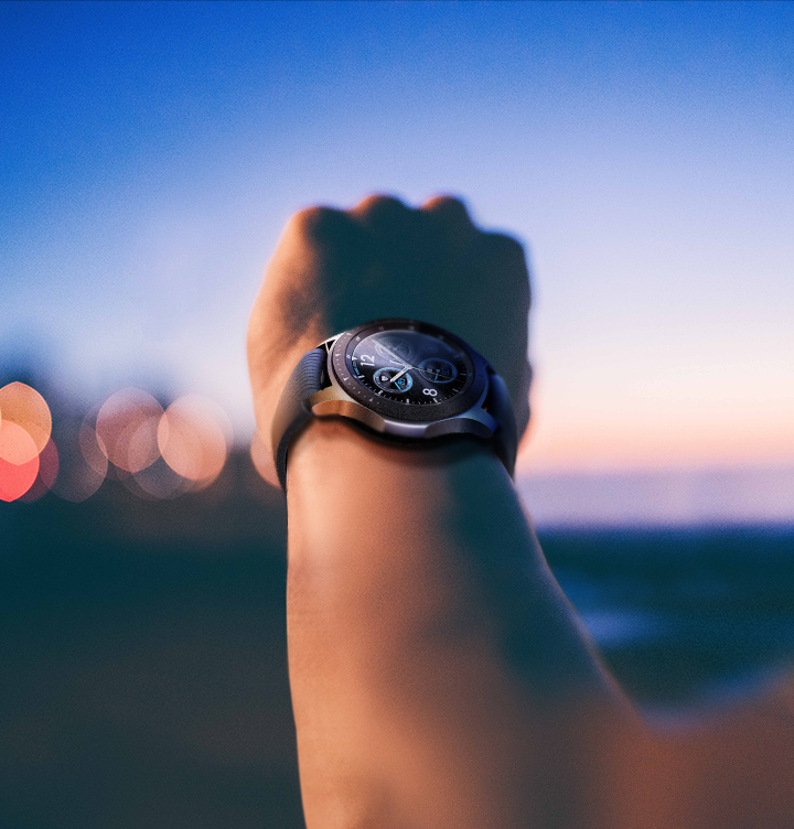 Das Handgelenk einer Person mit einer Smartwatch, die die Uhrzeit anzeigt, vor einem Sonnenuntergang.
