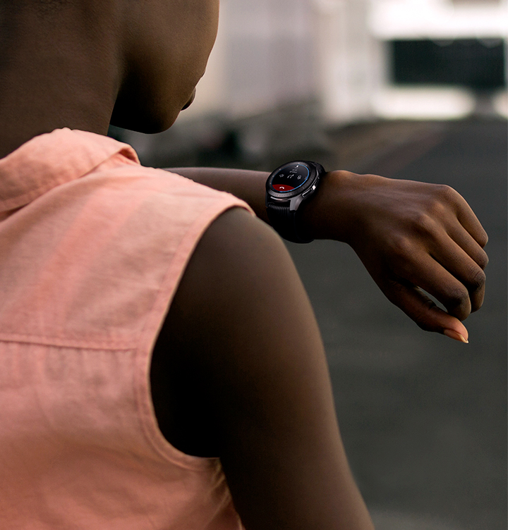 Eine Person mit rosa Hemd, die auf eine Smartwatch an ihrem Handgelenk blickt.