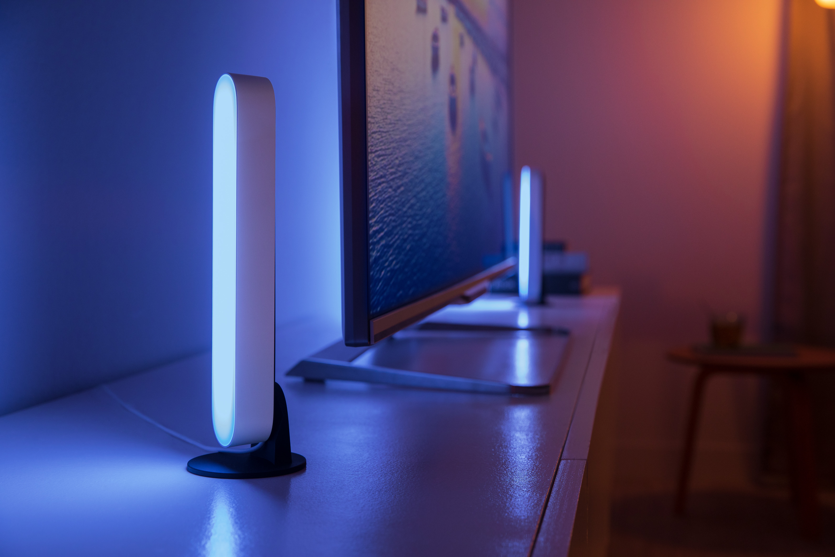 Zwei Lichtleisten neben einem Fernseher. Die Leisten emittieren blaues Licht, auf einer weißen Oberfläche.