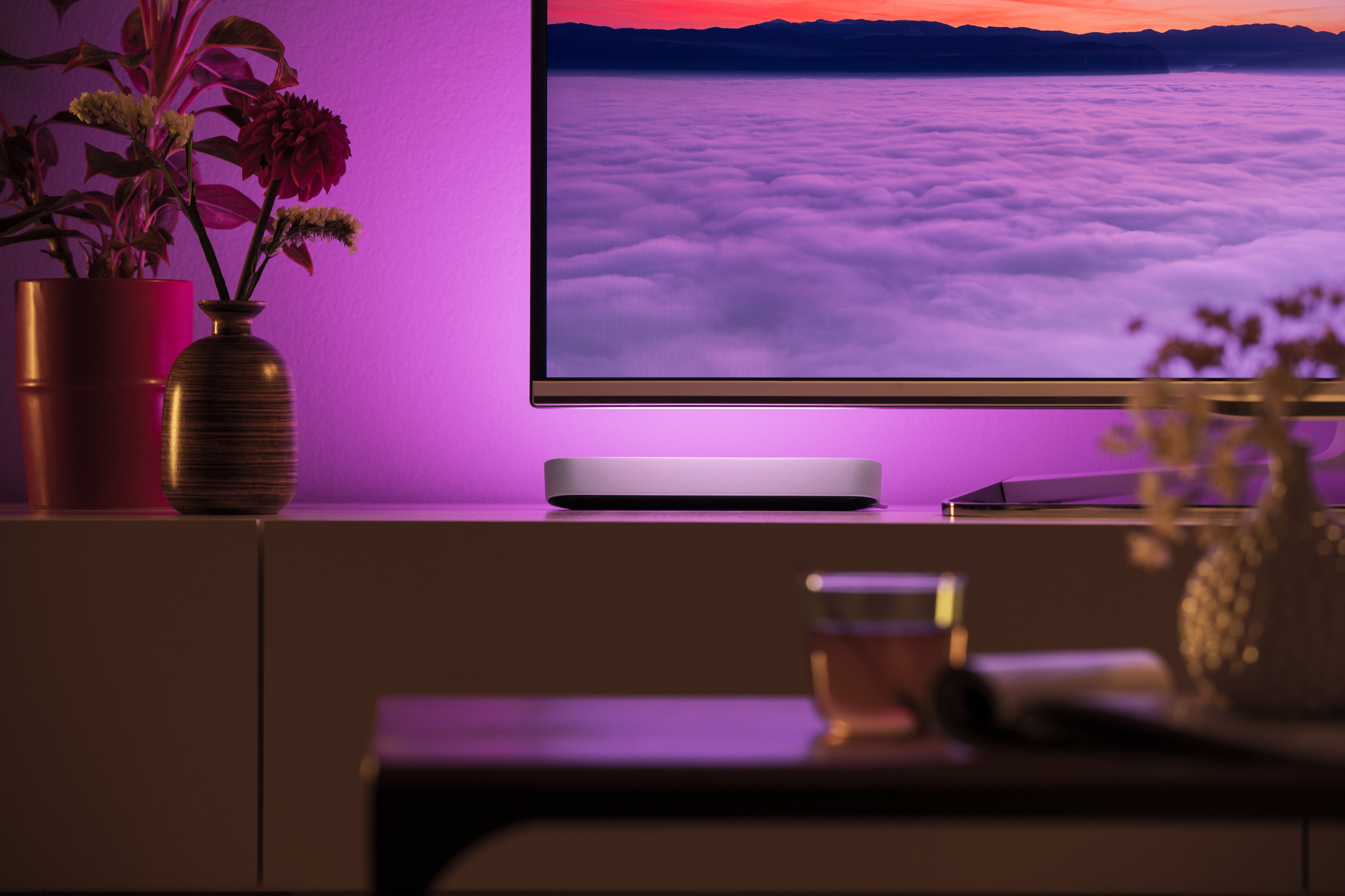 Fernseher mit farbigem Lichtstreifen auf einem weißen Schrank.