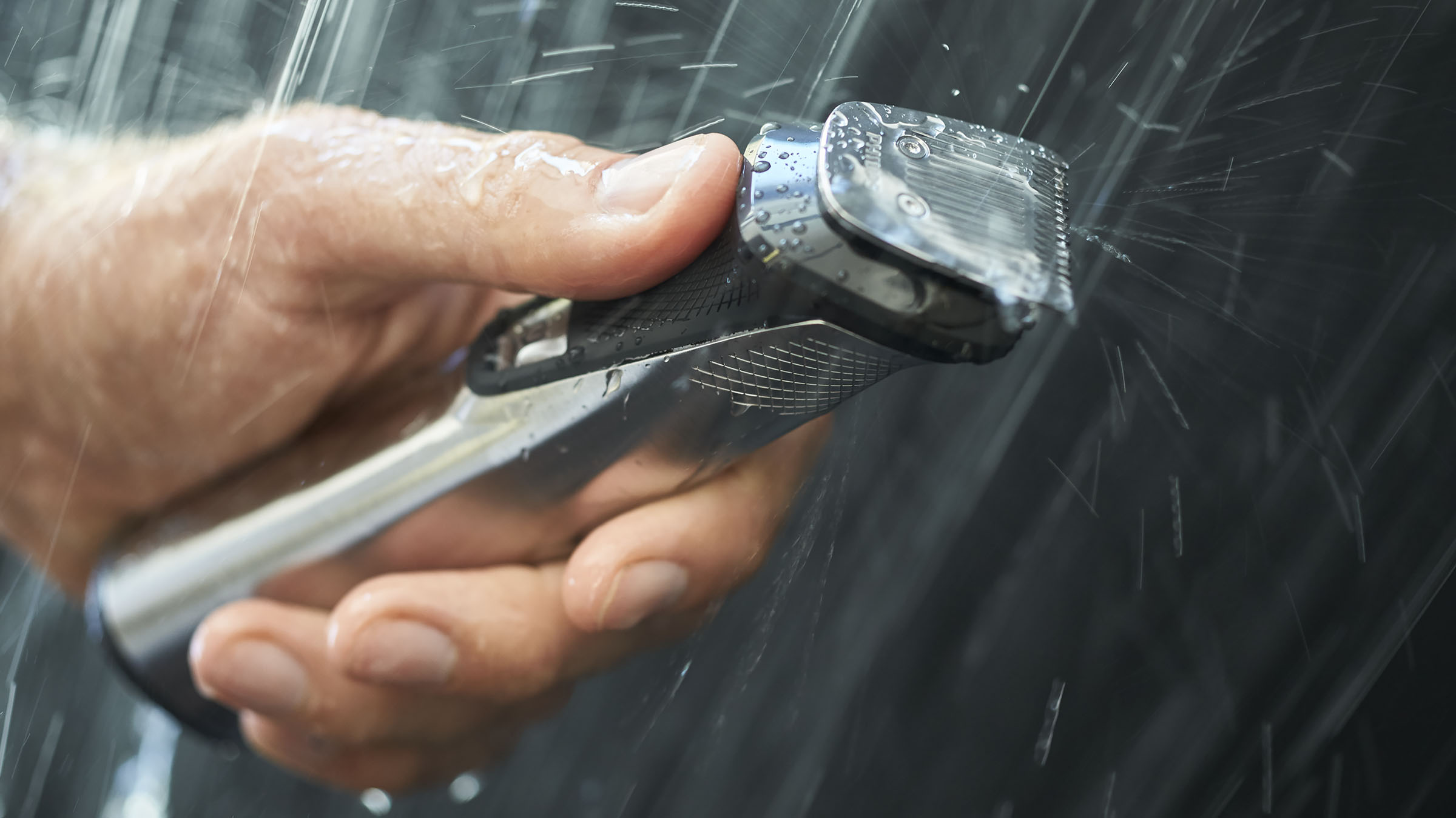 Hand hält schwarzen und silbernen Elektrorasierer unter Wasser.