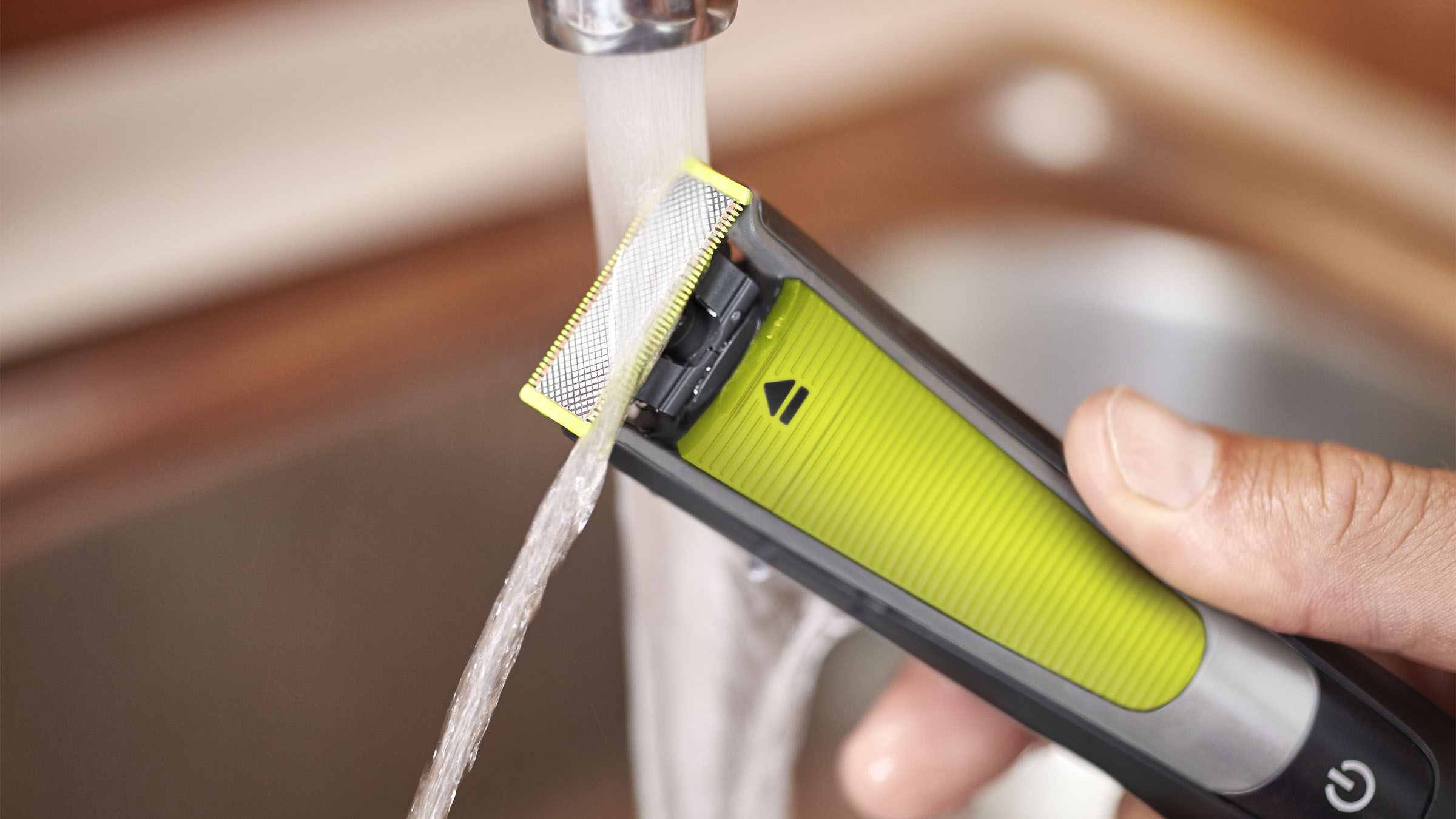Elektrischer Rasierer unter fließendem Wasser. Der Rasierer hat einen gelben und silbernen Kopf und einen schwarzen Griff.