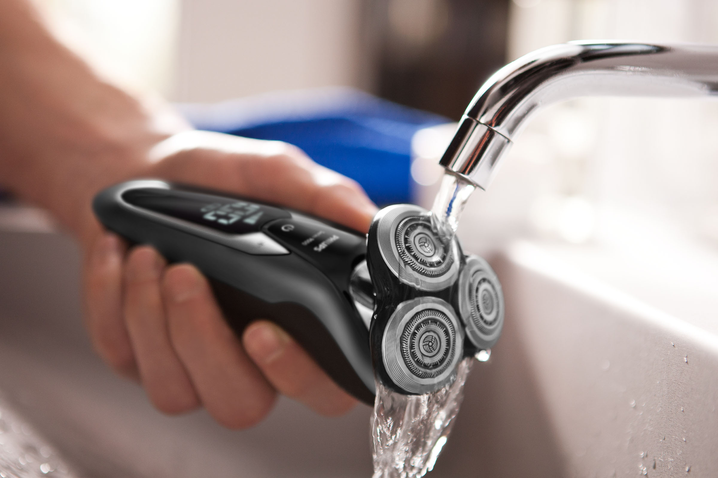 Ein Rasierer wird unter einem Wasserhahn gespült, Rasierköpfe sichtbar.