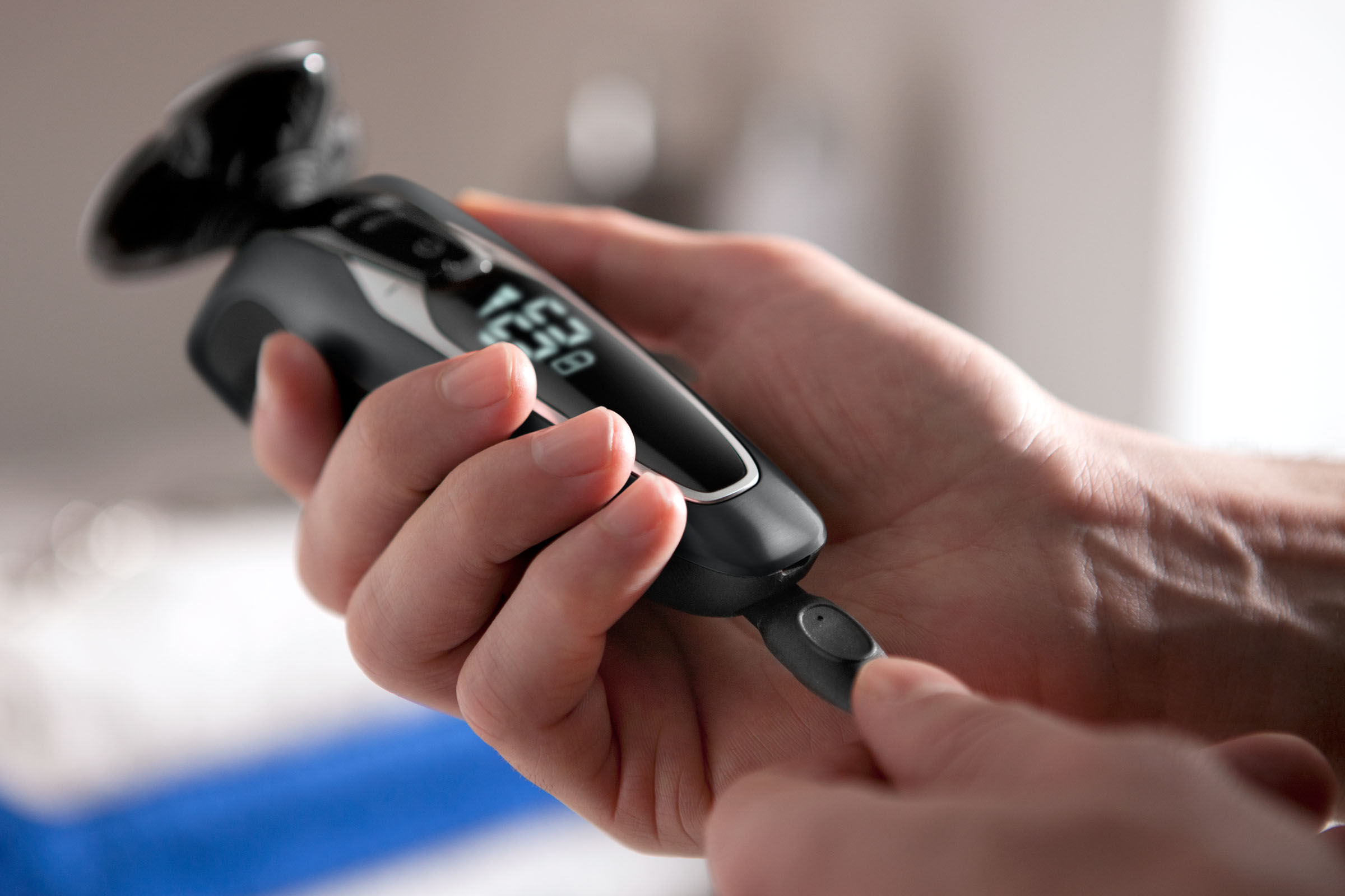 Eine Person hält einen schwarz-grauen Elektrorasierer, mit einem kleinen Trimmer verlängert.