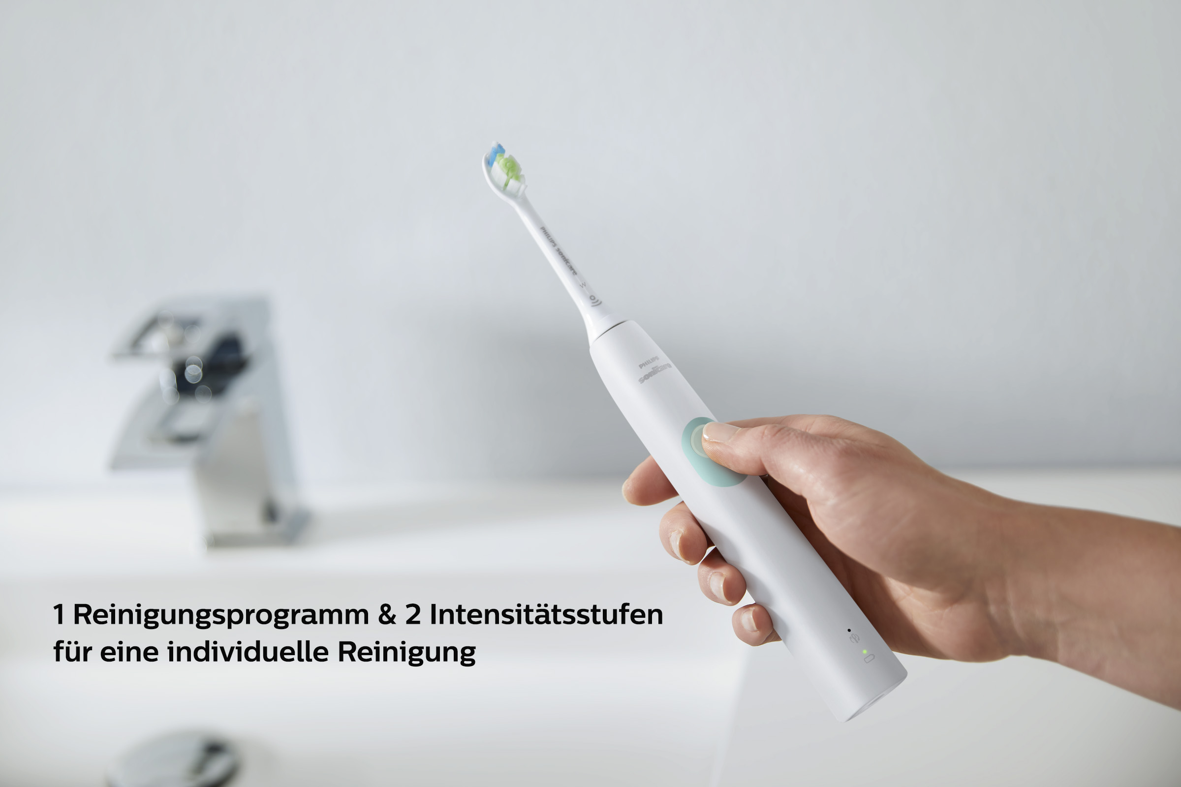 Eine Hand hält eine weiße elektrische Zahnbürste vor einem Waschbecken. Text: 1 Reinigungsprogramm & 2 Intensitäten.