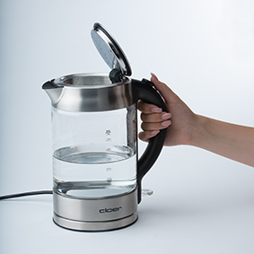 Person hält einen Glaskessel mit Wasser gefüllt. Der Deckel ist geöffnet.