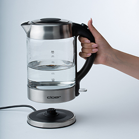 Ein Wasserkocher wird von seiner Basis abgehoben, das Wasser im Inneren zeigend. Hand hält den Kessel.