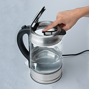 Hand drückt Knopf auf einem elektrischen Wasserkocher aus Glas, gefüllt mit Wasser.