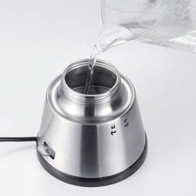 Wasser wird in einen Edelstahlkessel gegossen. Der Kessel steht auf einer weißen Oberfläche.