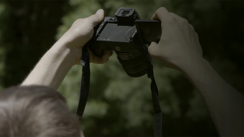 Egy személy fekete kamerát tart, a képernyő nyitva van, és a háttér elmosódott zöld.