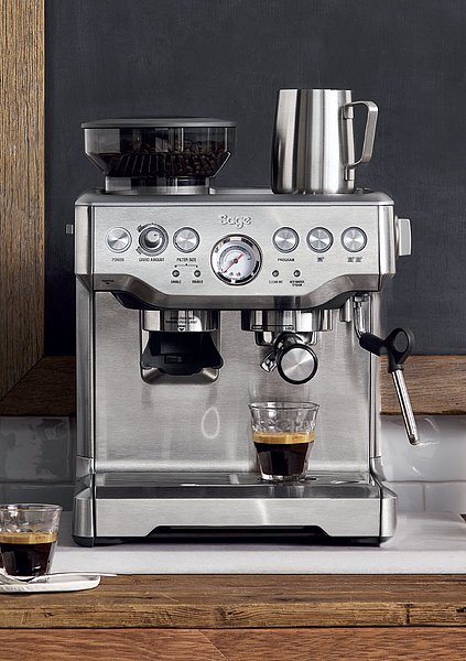 Silberfarbene Espressomaschine mit Mahlwerk und Milchaufschäumer. Zwei Espresso-Shots in Gläsern.