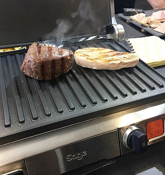Grill mit Steak und Hähnchenbrust. Der Grill ist heiß, Dampf steigt vom Essen auf.