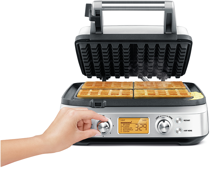 Ein offenes Waffeleisen mit Waffeln darin und eine Hand, die einen Drehregler einstellt.