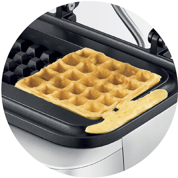 Ein Waffel wird in einem Waffeleisen gebacken, mit einem abgebrochenen Stück.