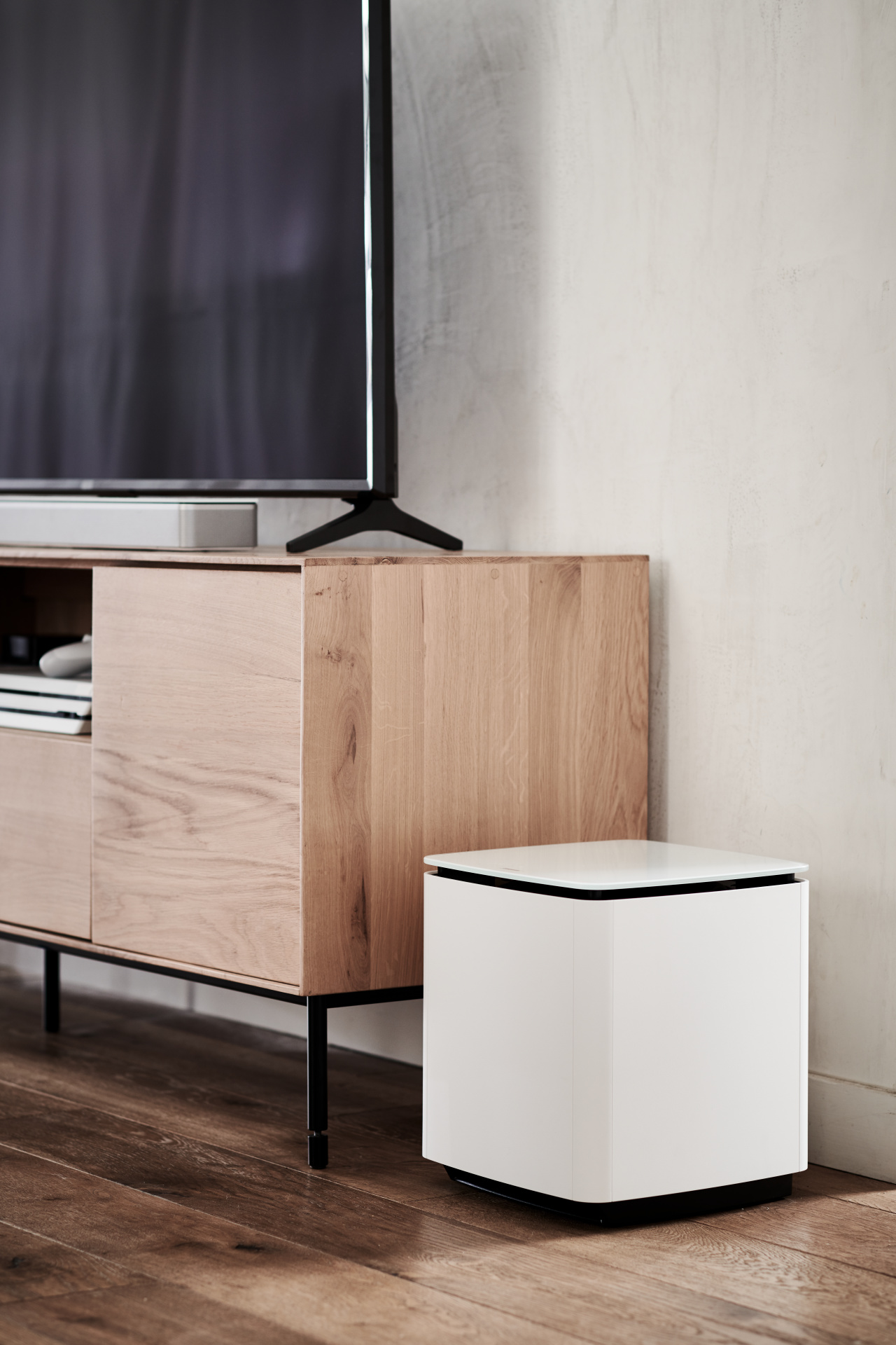 Modernes Wohnzimmer mit Holzschrank, weißem Subwoofer und Fernseher.